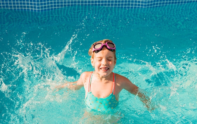 Gelukkig meisje zwemt in het zwembad. zomervakantie. meisje in een zwembroek en zwembril.