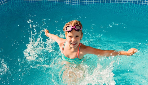 Gelukkig meisje zwemt in het zwembad. zomervakantie. meisje in een zwembroek en zwembril.