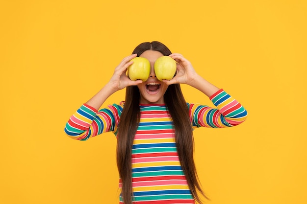 Gelukkig meisjeskind veel plezier met het houden van appelfruit op de gele achtergrond van de ogen, de gezondheid van het oog.
