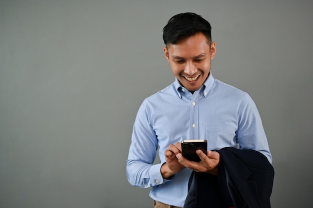 Gelukkig millennial Aziatische zakenman met behulp van zijn smartphone geïsoleerde grijze achtergrond