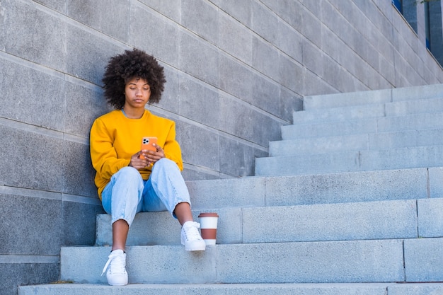 Gelukkig millennial gemengd ras meisje in de straat van de stad. Positieve jonge Afro-Amerikaanse vrouw surfen op het web, informatie zoeken, buiten winkelen in de online winkel