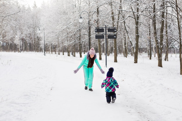 Gelukkig moeder en babymeisje op de wandeling in het besneeuwde winterbos.