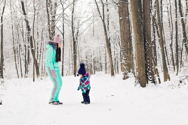 Gelukkig moeder en babymeisje op de wandeling in het besneeuwde winterbos.