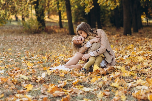 Gelukkig moeder en haar mooie dochter zitten en plezier maken tussen de gele bladeren in het herfstpark.