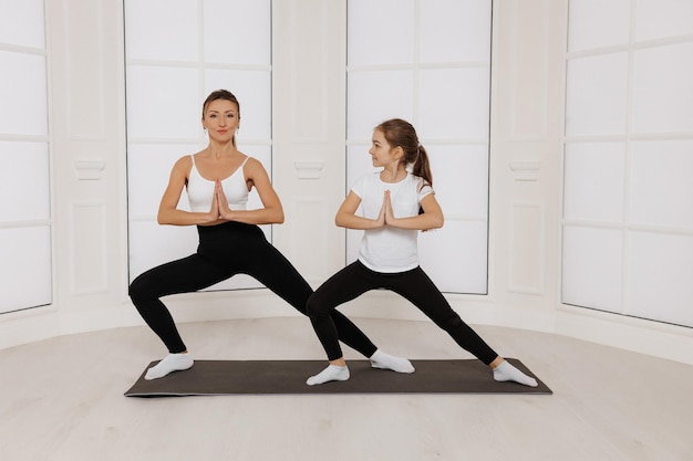 gelukkig moeder en kindmeisje dat yoga doet terwijl ze op de vloer in de sportschool staan