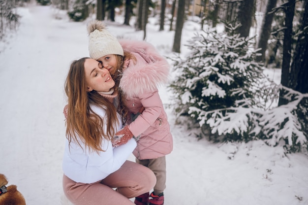 Gelukkig moeder en klein schattig meisje in roze warme uitloper wandelen met plezier en knuffelen in sneeuwwit