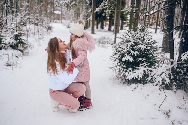 Gelukkig moeder en klein schattig meisje in roze warme uitloper wandelen met plezier en knuffelen in sneeuwwit