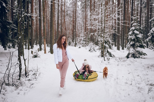 Gelukkig moeder en klein schattig meisje in roze warme uitloper wandelen plezier rijdt opblaasbare sneeuwbuis