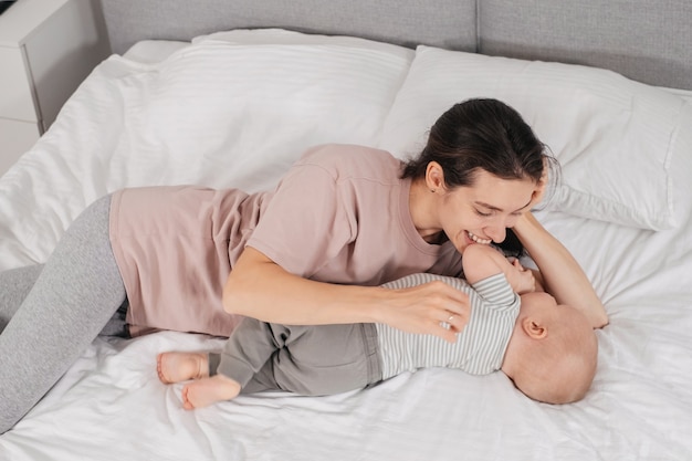 Gelukkig moeder met babyjongen knuffelen in bed thuis spelen