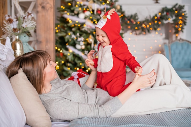 Gelukkig moeder spelen met haar peuter in rood santa rendier kostuum op kerstboom achtergrond