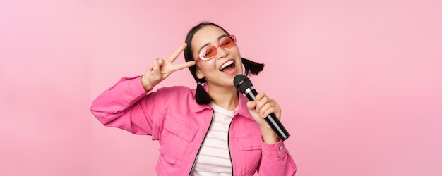 Gelukkig mooi Aziatisch meisje zingen met microfoon met behulp van microfoon genieten van karaoke poseren tegen roze studio achtergrond