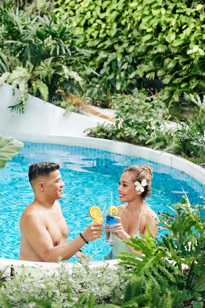 Gelukkig mooi Aziatisch stel flirt en drinkt smakelijke cocktails wanneer ze in het zwembad van het hotel staan