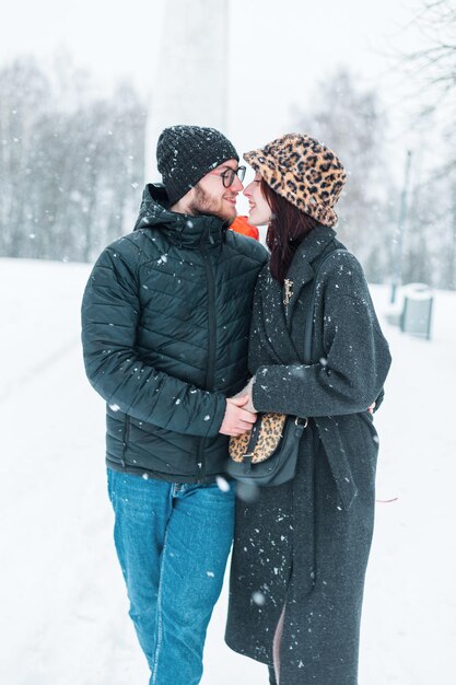 gelukkig mooi jong meisje en een knap model jongen in modieuze winterkleding lopen samen in een park met sneeuw mooi verliefd paar