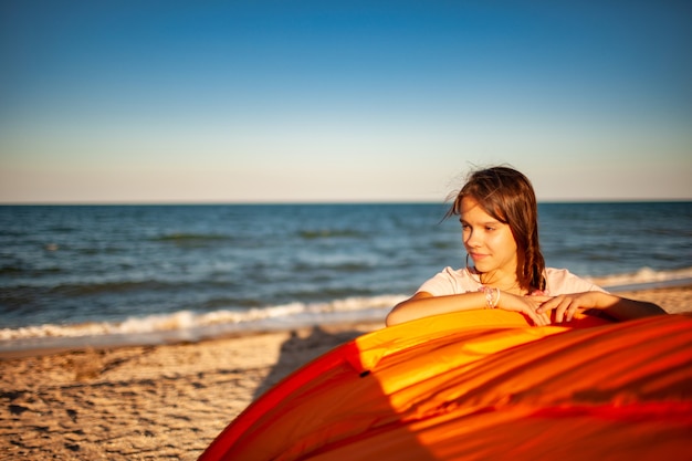 Gelukkig mooi jong meisje met donker haar staat in de buurt van een lichte tent lachend op het zandstrand van de blauwe glanzende zee