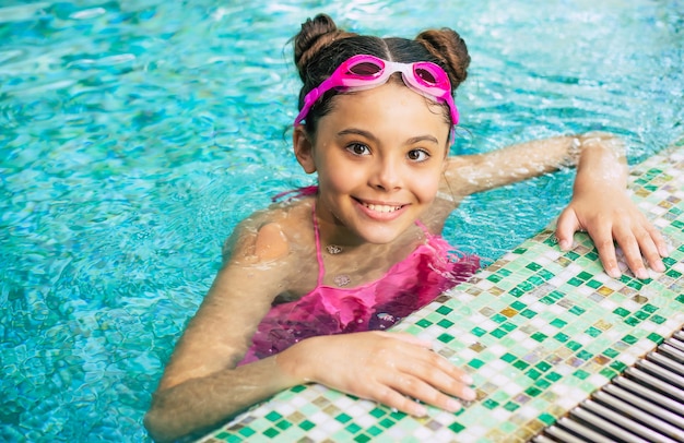 Gelukkig mooi klein glimlachend meisje in bril en zwembroek in het zwembad heeft plezier tijdens vakantie of zwemlessen.