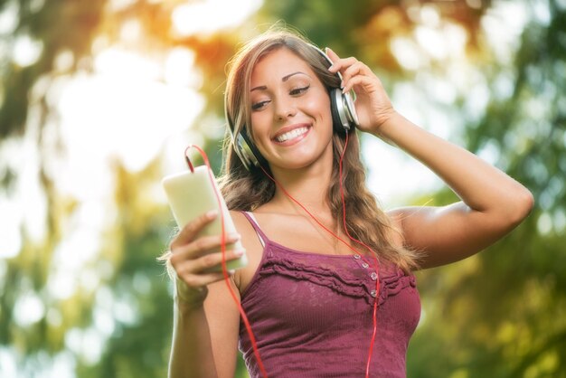 Gelukkig mooi meisje in het park en muziek luisteren van slimme telefoon.