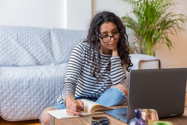 Gelukkig mooi meisje zit en maakt gebruik van haar grijze computer Achter haar staat een witte fauteuil met een groen kussen en een plant