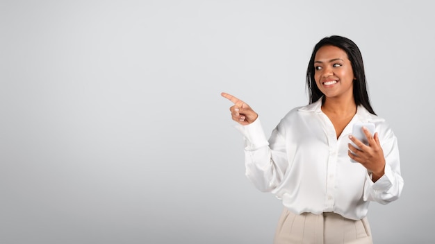 Gelukkig mooi millennial zwart vrouwtje in witte blouse typen op smartphone met vinger op vrije ruimte