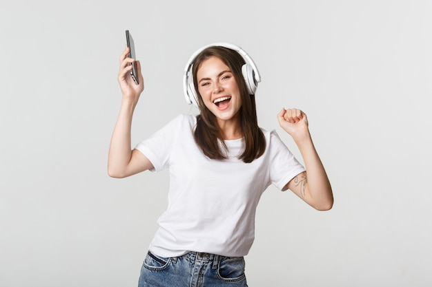 Gelukkig mooie brunette meisje dansen en luisteren muziek in draadloze hoofdtelefoons, smartphone te houden.