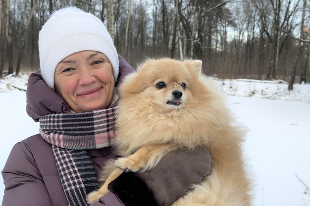 Gelukkig mooie dame gepensioneerd oudere senior vrouw loopt met haar Pommerse Spitz hond op koude winterdag in de sneeuw