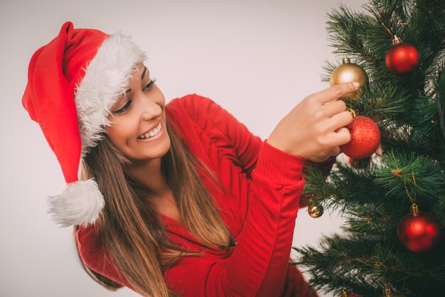 Gelukkig mooie jonge vrouw kerstboom versieren met rode sieraad thuis.