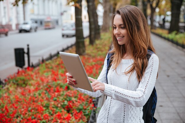 Gelukkig mooie jonge vrouw met rugzak met behulp van tablet in park