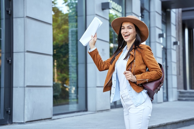 Gelukkig mooie jonge vrouw met rugzak zwaaiende hand in de stad. Lifestyle-concept