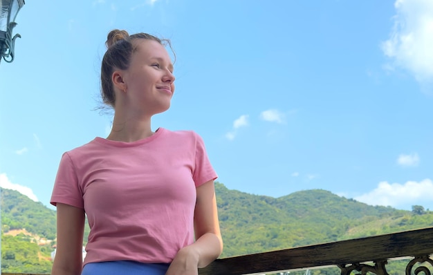 Gelukkig mooie jonge vrouw staan op balkon thuis op zonnige zomerdag met natuurlijke achtergrond genieten van zonnige zomerdag naar buiten kijken