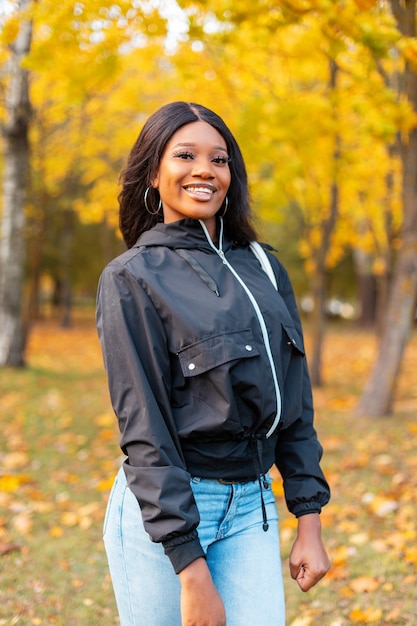 Gelukkig mooie lachende Afro-Amerikaanse vrouw in mode casual kleding wandelen in herfst kleurrijk park