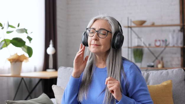 Gelukkig mooie oudere grijsharige vrouw in zwarte koptelefoon genieten van favoriete muziek luisteren.