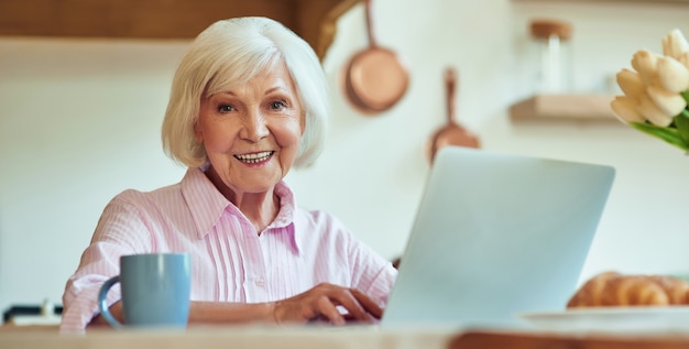 Gelukkig mooie senior vrouw zittend op de keuken met gadget