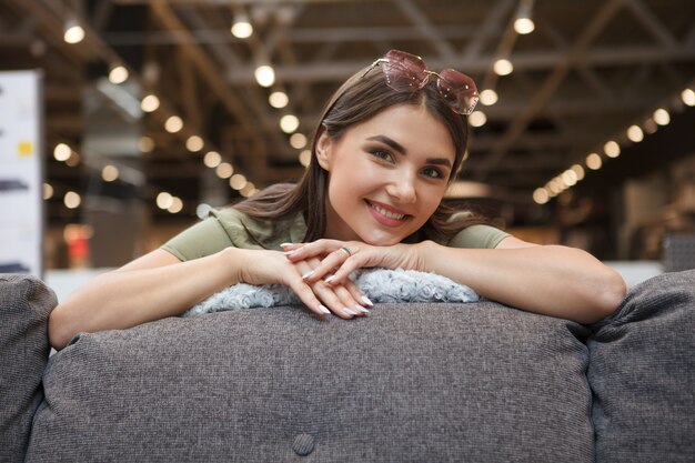 Gelukkig mooie vrouw lachend naar de camera, zittend op een nieuwe bank te koop bij meubelwinkel