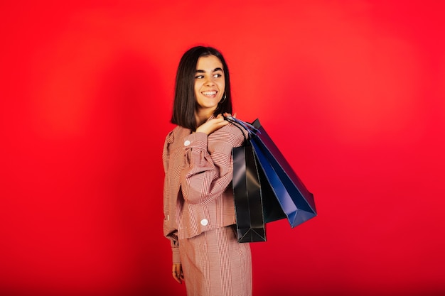 Gelukkig mooie vrouw met boodschappentassen geïsoleerd over rode muur