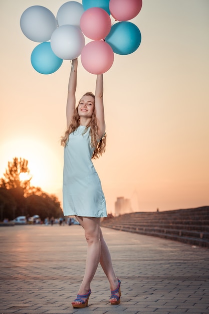 Gelukkig mooie vrouw met vliegende veelkleurige ballonnen bij zonsondergang.