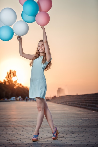 Gelukkig mooie vrouw met vliegende veelkleurige ballonnen bij zonsondergang.