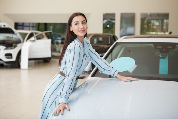 Gelukkig mooie vrouw poseren met haar nieuwe auto bij autodealer