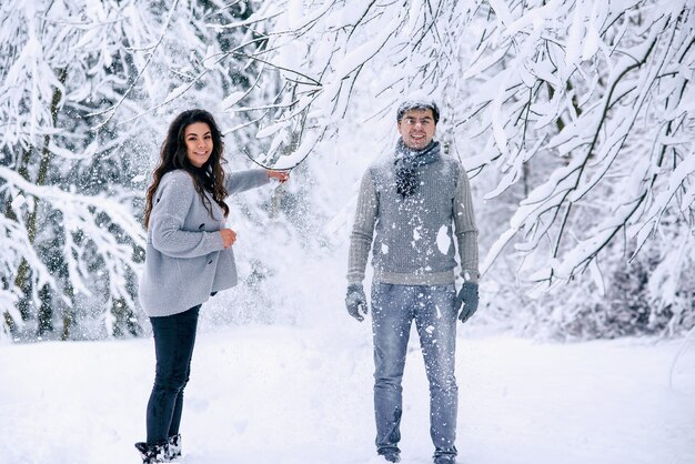 Gelukkig mooie zwangere vrouw in warme kleren gooit sneeuw op haar man