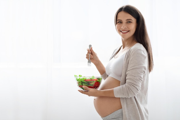 Gelukkig mooie zwangere vrouw met kom met verse groentesalade