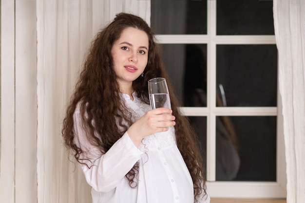 Gelukkig mooie zwangere vrouw met lang donkerbruin haar, met grote buik, met een glas water in de hand