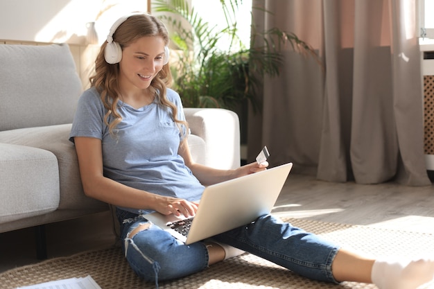 Gelukkig natuurlijke blonde met creditcard en laptop in de woonkamer.