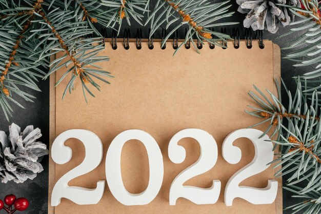 Foto gelukkig nieuwjaar 2022. witte cijfers 2022 liggend op gevouwen notitieboekje met kerstboomtakken en dennenappels, kopieer ruimte