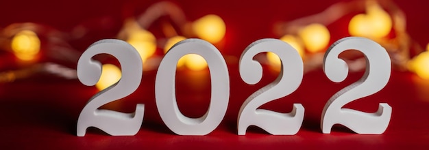 Gelukkig Nieuwjaar 2022. Witte houten nummers 2022 staan op rode achtergrond met slinger gloeilampen, vrolijk kerstfeest.