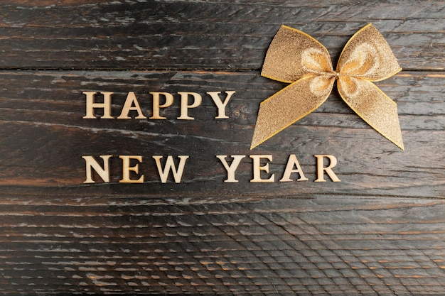 Foto gelukkig nieuwjaar houten tekst en gouden strik op een houten achtergrond feestelijke wenskaart met kopieerruimte