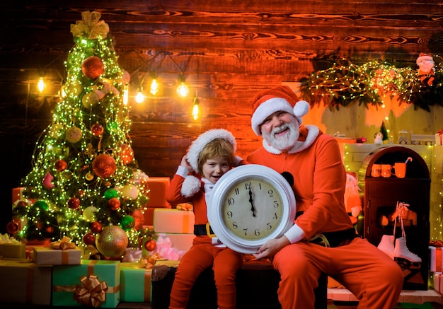 Gelukkig nieuwjaar kerstman met kleine assistent houdt oude klok jongen jongen verkleed als de kerstman wacht