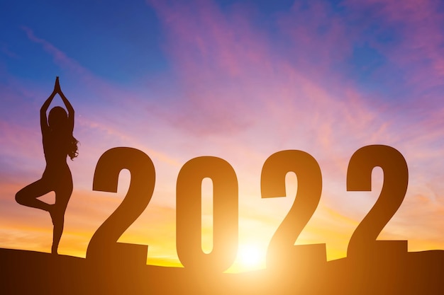 Gelukkig Nieuwjaar nummers 2022, silhouet vrouw beoefenen van yoga vroege ochtend zonsopgang boven de horizon achtergrond, gezondheid en gelukkig nieuwjaar concept.