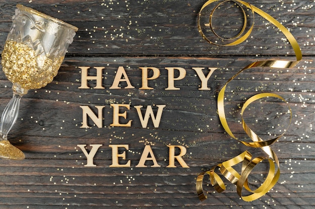 Foto gelukkig nieuwjaar wenskaart glas champagne en serpantine van gouden kleur op houten tafel met verspreide confetti