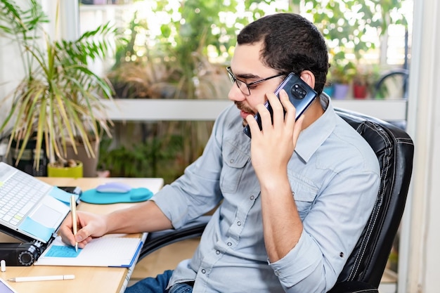 Gelukkig ondernemer praten op mobiele telefoon tijdens het schrijven op kladblok op kantoor