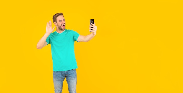 Gelukkig ongeschoren jonge man selfie maken op telefoon op gele achtergrond communicatie