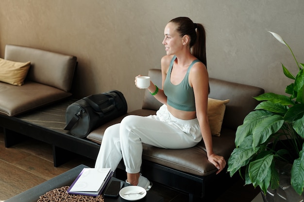 Foto gelukkig ontspannen meisje met kopje thee zittend op de bank in de lounge