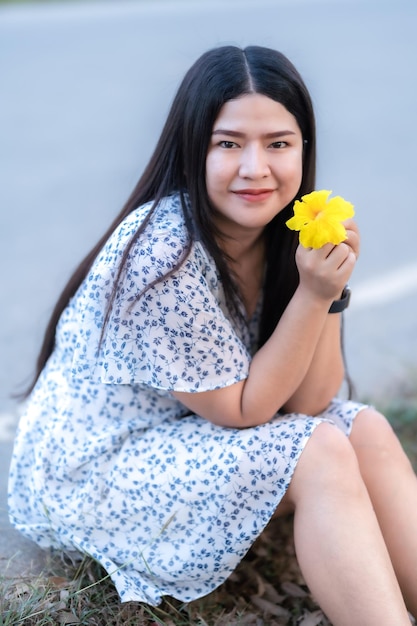 Gelukkig ontspannend portret aziatische vrouw in mooie bloeiende gele gouden tabebuia chrysotricha bloemen met het park in lentedag bij avondachtergrond in thailand